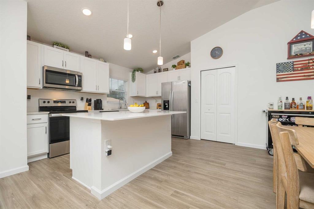 A kitchen features white cabinets, stainless steel appliances, a center island, and wood-look flooring — 42 WOODBORN LANE, PALM COAST, FL
