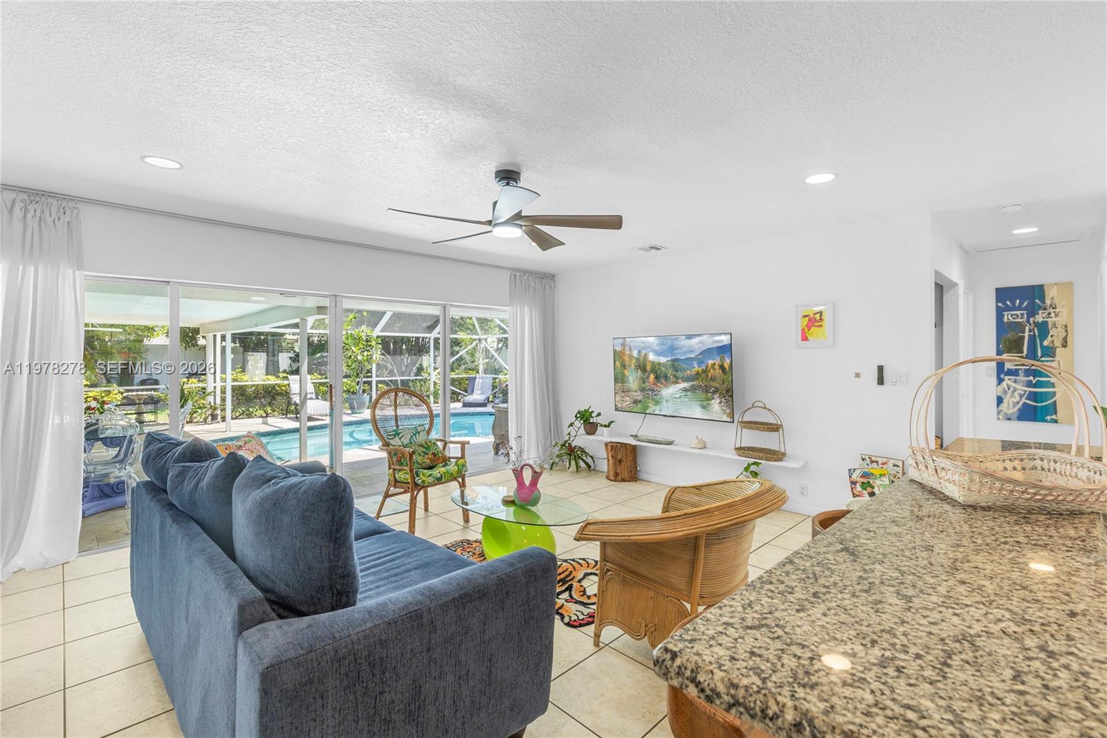 A living room features a blue sofa, wicker chairs, a glass coffee table, and pool views — 809 SE 14th Dr, Deerfield Beach FL 33441, DEERFIELD BEACH, FL