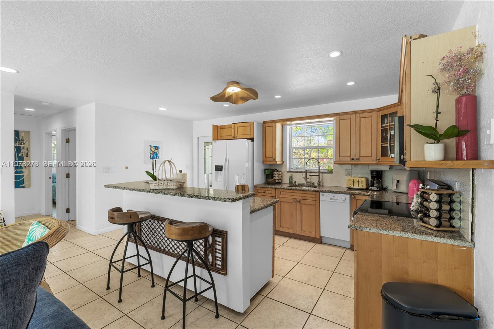 A kitchen features light wood cabinets, granite countertops, tile flooring, and a breakfast bar — 809 SE 14th Dr, Deerfield Beach FL 33441, DEERFIELD BEACH, FL