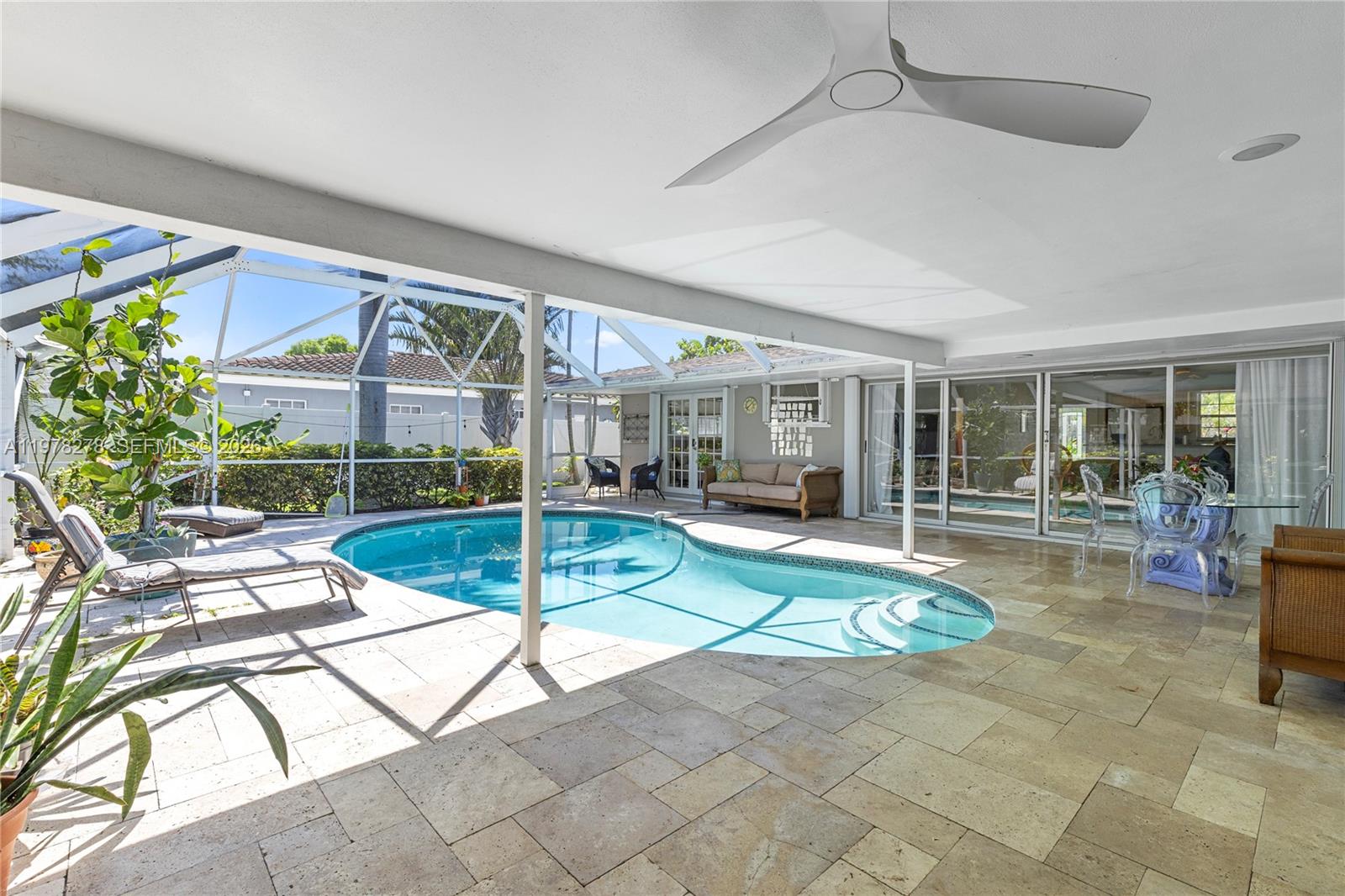 A covered patio with stone flooring overlooks a screened-in swimming pool and backyard — 809 SE 14th Dr, Deerfield Beach FL 33441, DEERFIELD BEACH, FL