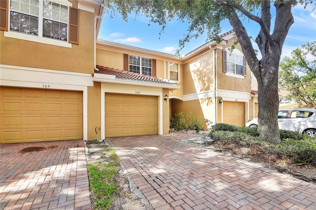 A row of tan townhouses features brick-paved driveways, garage doors, and a large shade tree — 6480 RANELAGH DRIVE UNIT 106, ORLANDO, FL