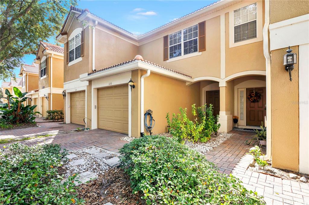 The exterior of a two-story tan townhouse features a garage, a front entrance, and landscaping — 6480 RANELAGH DRIVE UNIT 106, ORLANDO, FL