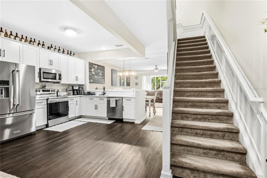 A kitchen with white cabinets and stainless steel appliances sits beside a carpeted staircase — 6480 RANELAGH DRIVE UNIT 106, ORLANDO, FL