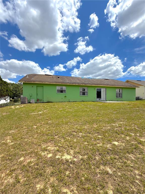 The exterior rear view of a lime green house with a shingled roof and yard — 7755 BAY CEDAR DRIVE, ORLANDO, FL
