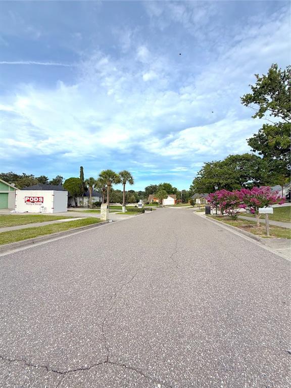 A residential street view featuring a PODS container, palm trees, and blooming bushes — 7755 BAY CEDAR DRIVE, ORLANDO, FL