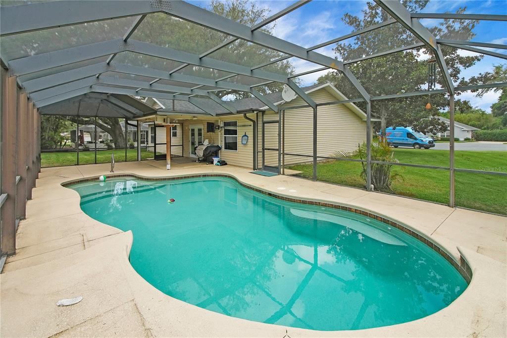 A screened-in patio features a kidney-shaped swimming pool next to a single-story house — 1204 OAK HAMMOCK LANE, LADY LAKE, FL