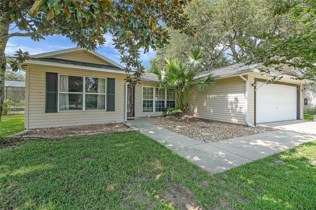 A single-story house with beige siding, a two-car garage, and a front walkway — 1204 OAK HAMMOCK LANE, LADY LAKE, FL