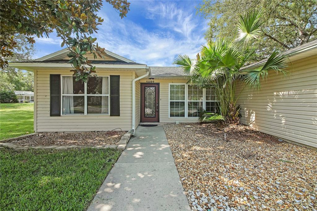 A single-story house with beige siding, a concrete walkway, and a palm tree in front — 1204 OAK HAMMOCK LANE, LADY LAKE, FL