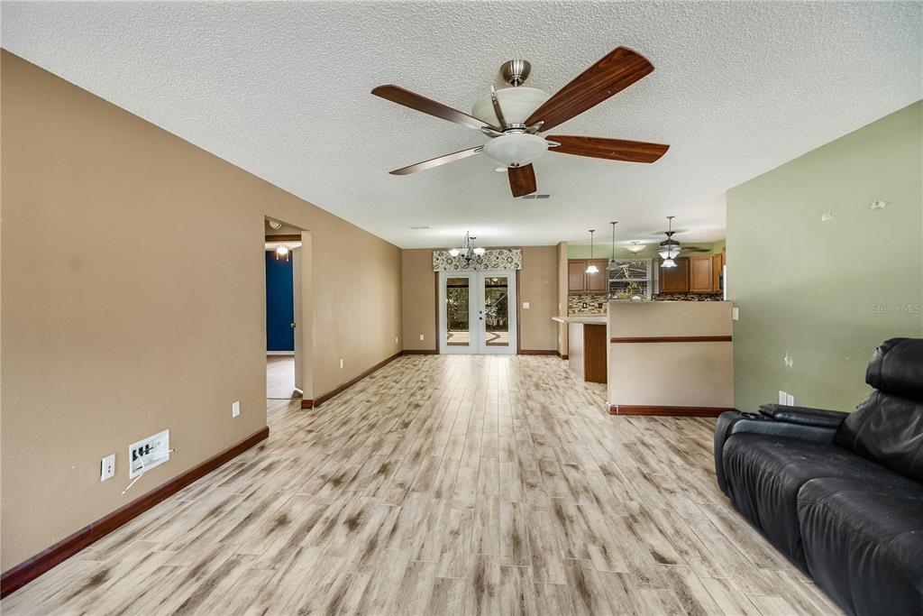 A living room with wood-look tile flooring, a ceiling fan, and an adjacent kitchen area — 1204 OAK HAMMOCK LANE, LADY LAKE, FL
