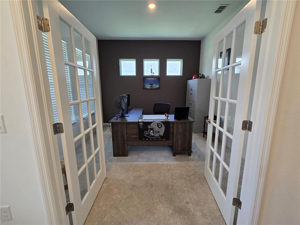 A home office features a wooden desk, gray carpet, and double French doors — 863 W BAYSHORE DRIVE, TARPON SPRINGS, FL
