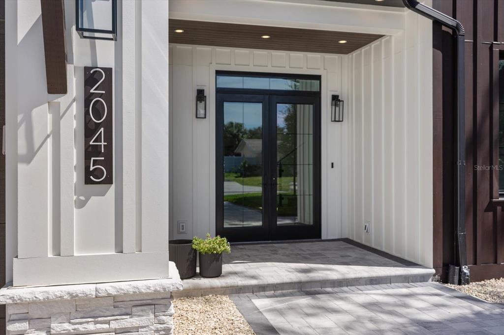 A modern home entrance features a black double door, white vertical siding, and stone accents — 2045 GOLDENROD STREET, SARASOTA, FL