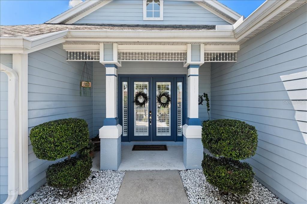 The front entrance features double glass doors, two topiary bushes, and light blue siding — 4748 COMPASS DRIVE, BRADENTON, FL