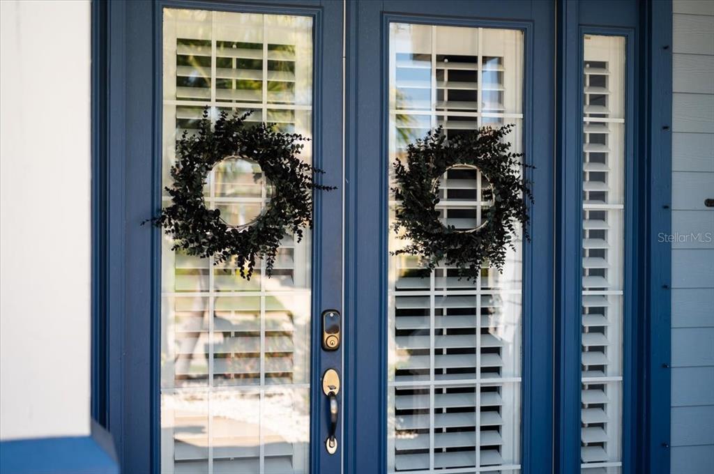 A pair of blue double doors with glass panels, white shutters, and matching decorative wreaths — 4748 COMPASS DRIVE, BRADENTON, FL