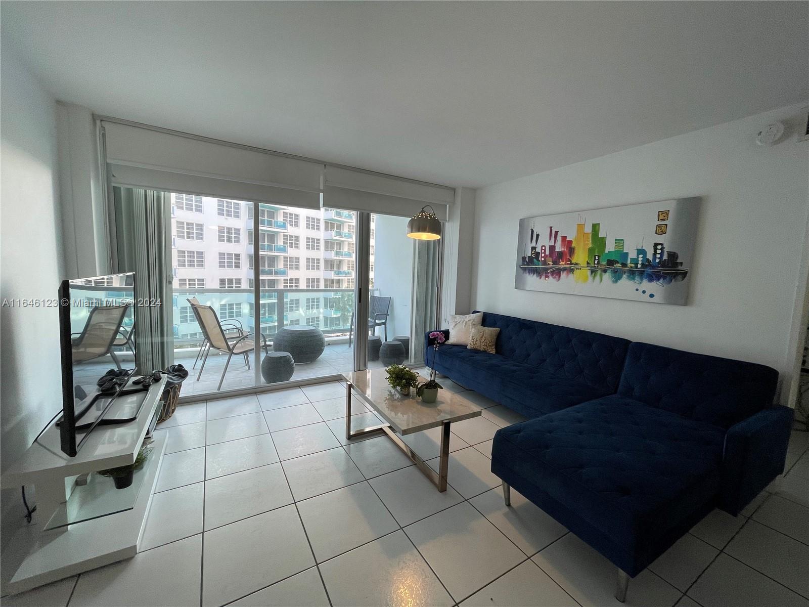 A living room features a blue sectional sofa, a coffee table, and a balcony view — 5151 Collins Ave # 629, Miami Beach FL 33140, MIAMI BEACH, FL