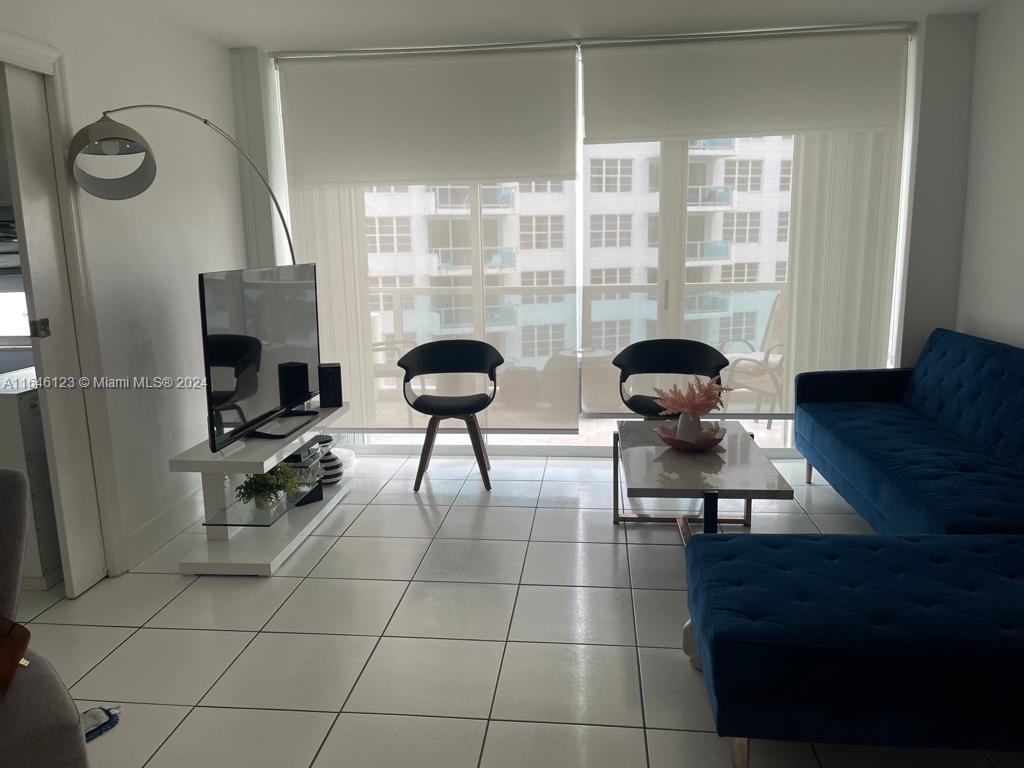 A living room features a blue sofa, a white TV stand, and floor-to-ceiling windows — 5151 Collins Ave # 629, Miami Beach FL 33140, MIAMI BEACH, FL