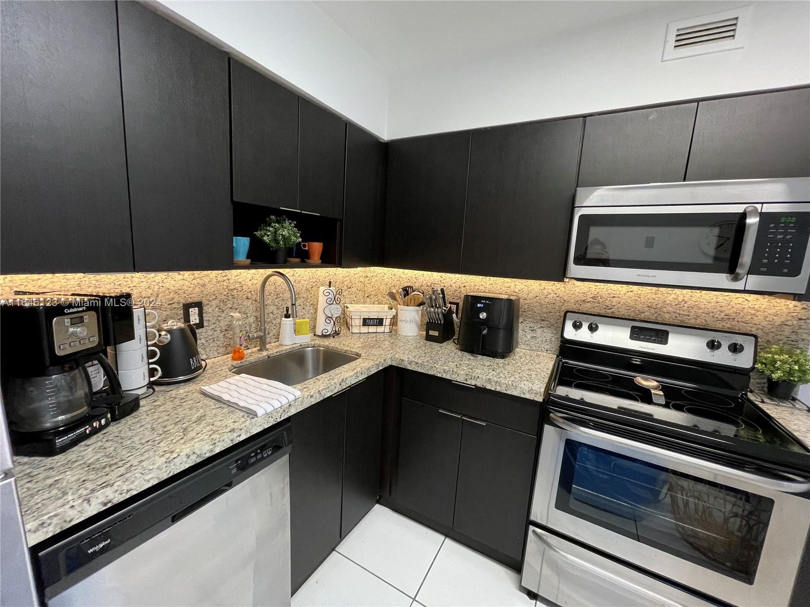 A kitchen features dark cabinets, granite countertops, stainless steel appliances, and under-cabinet lighting — 5151 Collins Ave # 629, Miami Beach FL 33140, MIAMI BEACH, FL
