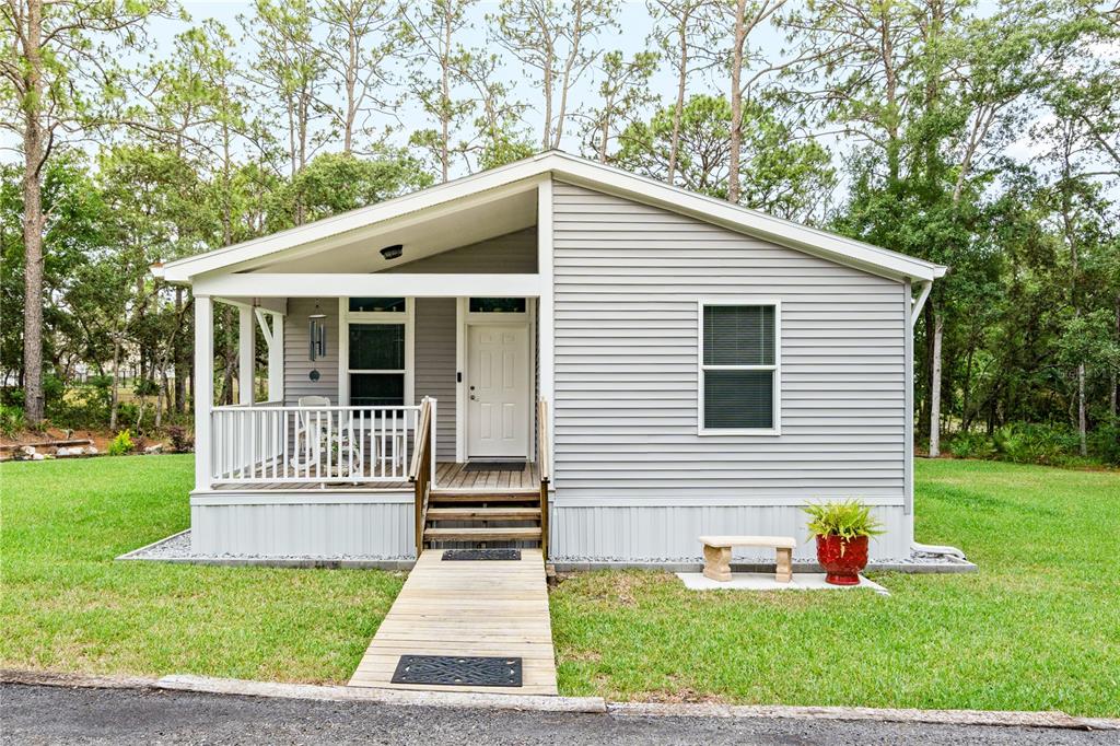 A small, gray-sided house with a front porch, wooden ramp, and surrounding lawn — 7039 S STRAIGHT AVENUE, HOMOSASSA, FL