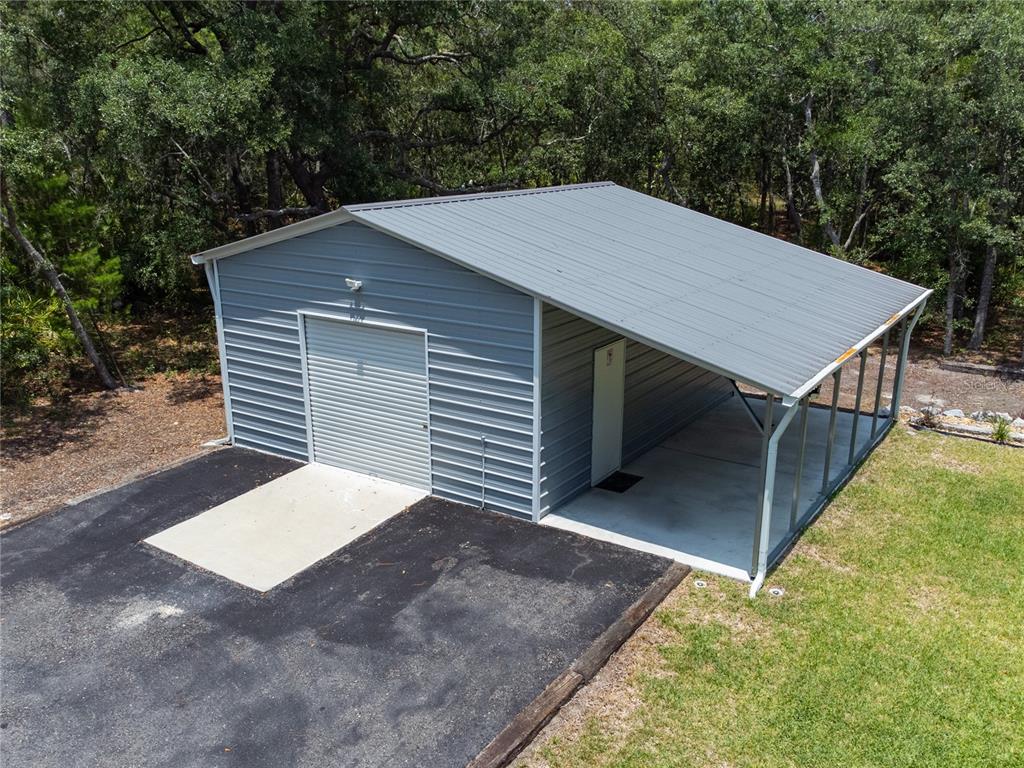 A metal garage with a roll-up door and an attached carport sits on a concrete pad — 7039 S STRAIGHT AVENUE, HOMOSASSA, FL