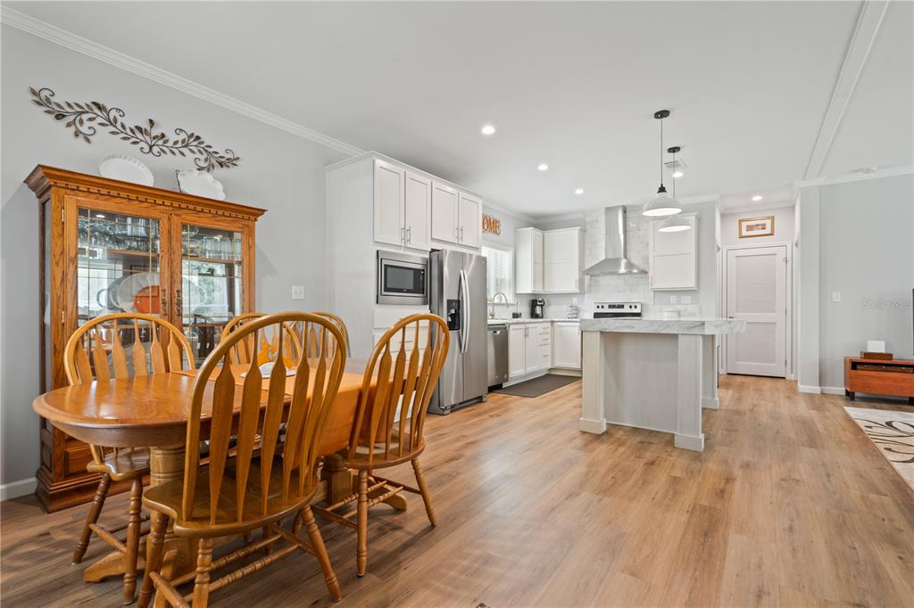 A dining area with a wooden table and hutch opens into a modern white kitchen — 7039 S STRAIGHT AVENUE, HOMOSASSA, FL