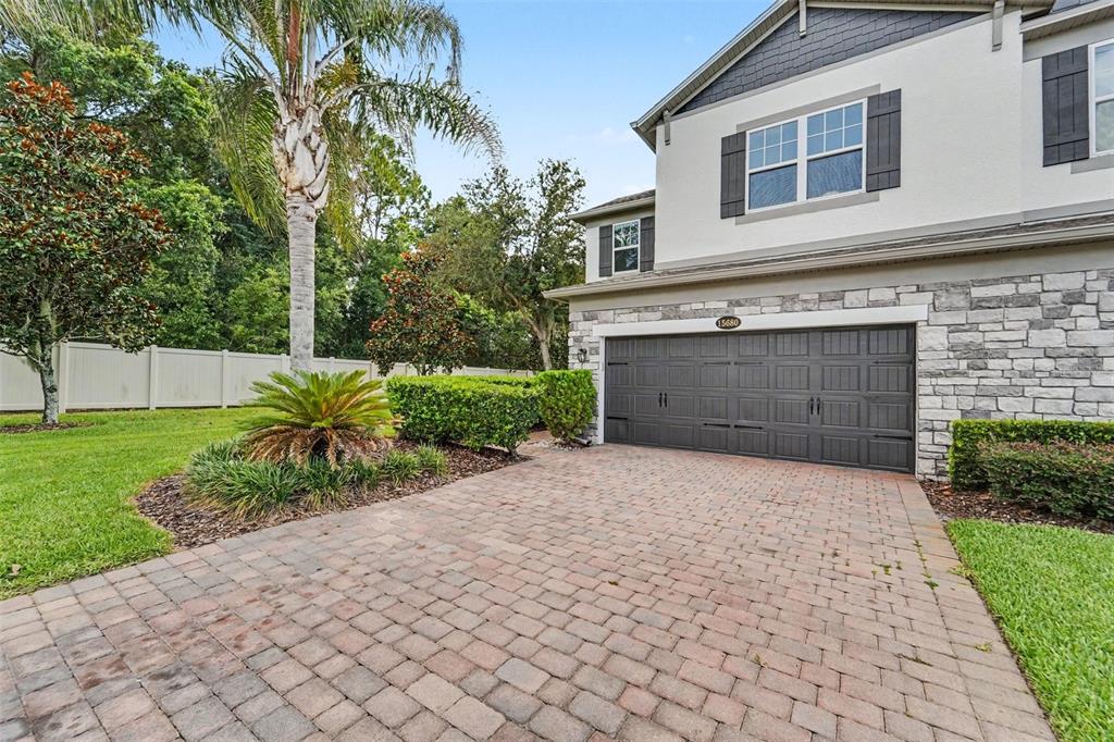 A two-story house exterior features a stone facade, a dark garage door, and a driveway — 15680 ORANGE HARVEST LOOP, WINTER GARDEN, FL