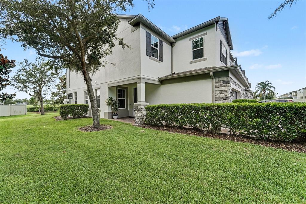 A two-story townhouse exterior features a stone-accented entrance, a manicured hedge, and a grassy lawn — 15680 ORANGE HARVEST LOOP, WINTER GARDEN, FL