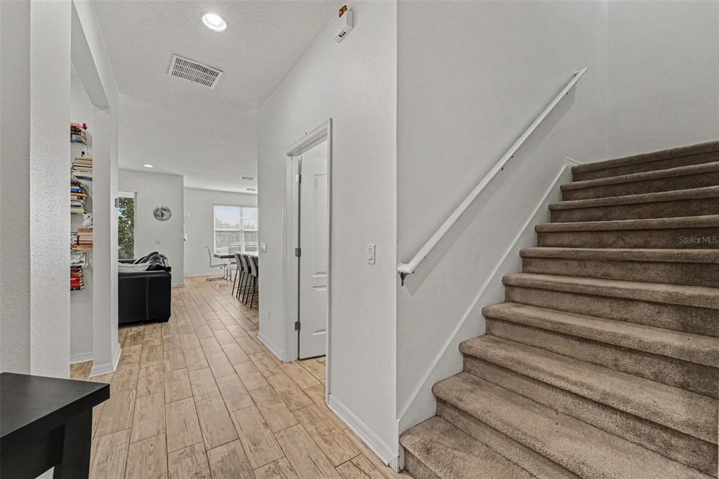 A carpeted staircase sits beside a hallway leading to a living area with wood-look flooring — 15680 ORANGE HARVEST LOOP, WINTER GARDEN, FL