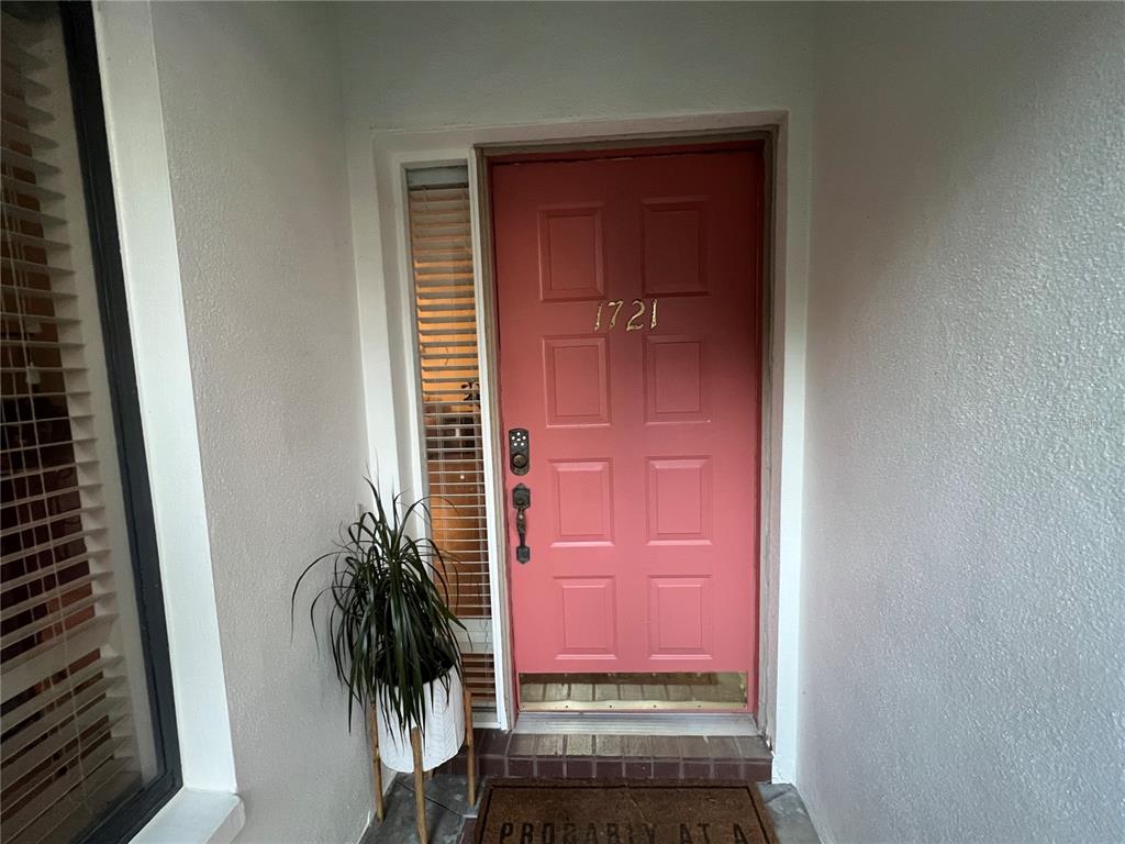 A coral-colored front door with a side window and a potted plant sits under an entryway — 1721 LAKE CYPRESS DRIVE UNIT 2101, SAFETY HARBOR, FL