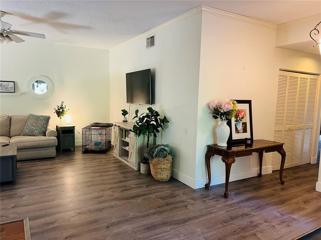 A living room features light wood-look flooring, a wall-mounted television, and a wooden console table — 1721 LAKE CYPRESS DRIVE UNIT 2101, SAFETY HARBOR, FL