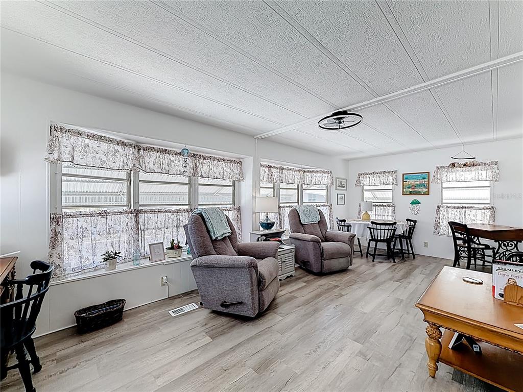 A living and dining area features wood-look flooring, two grey recliners, and large windows — 665 54TH STREET S UNIT 133, GULFPORT, FL
