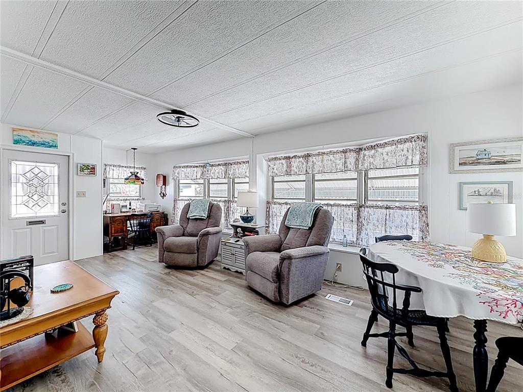 A living and dining area features light wood flooring, two gray recliners, and white walls — 665 54TH STREET S UNIT 133, GULFPORT, FL