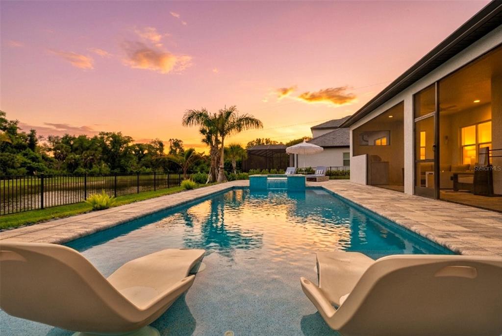 A swimming pool with lounge chairs sits on a patio overlooking a sunset landscape — 1154 KINGS WAY DRIVE, NOKOMIS, FL