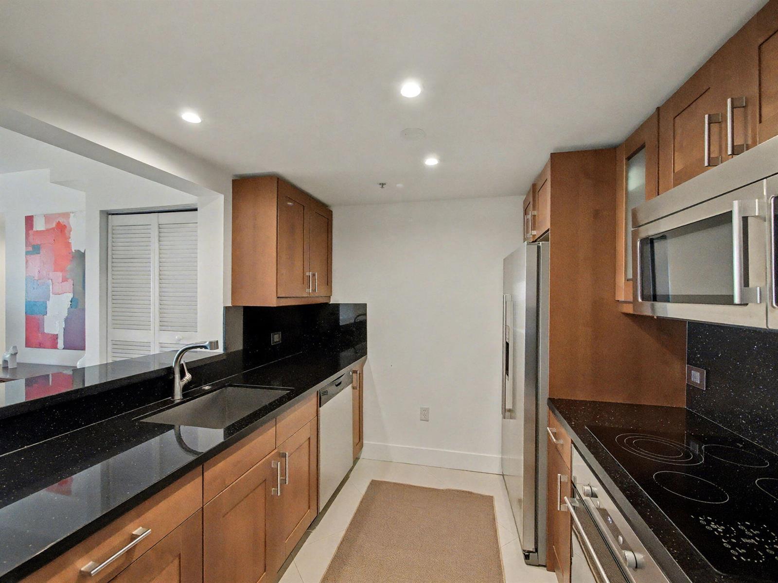 A kitchen features wood cabinets, black countertops, stainless steel appliances, and a pass-through window — 2600 SW 27th Avenue # 603, Miami FL 33133, MIAMI, FL
