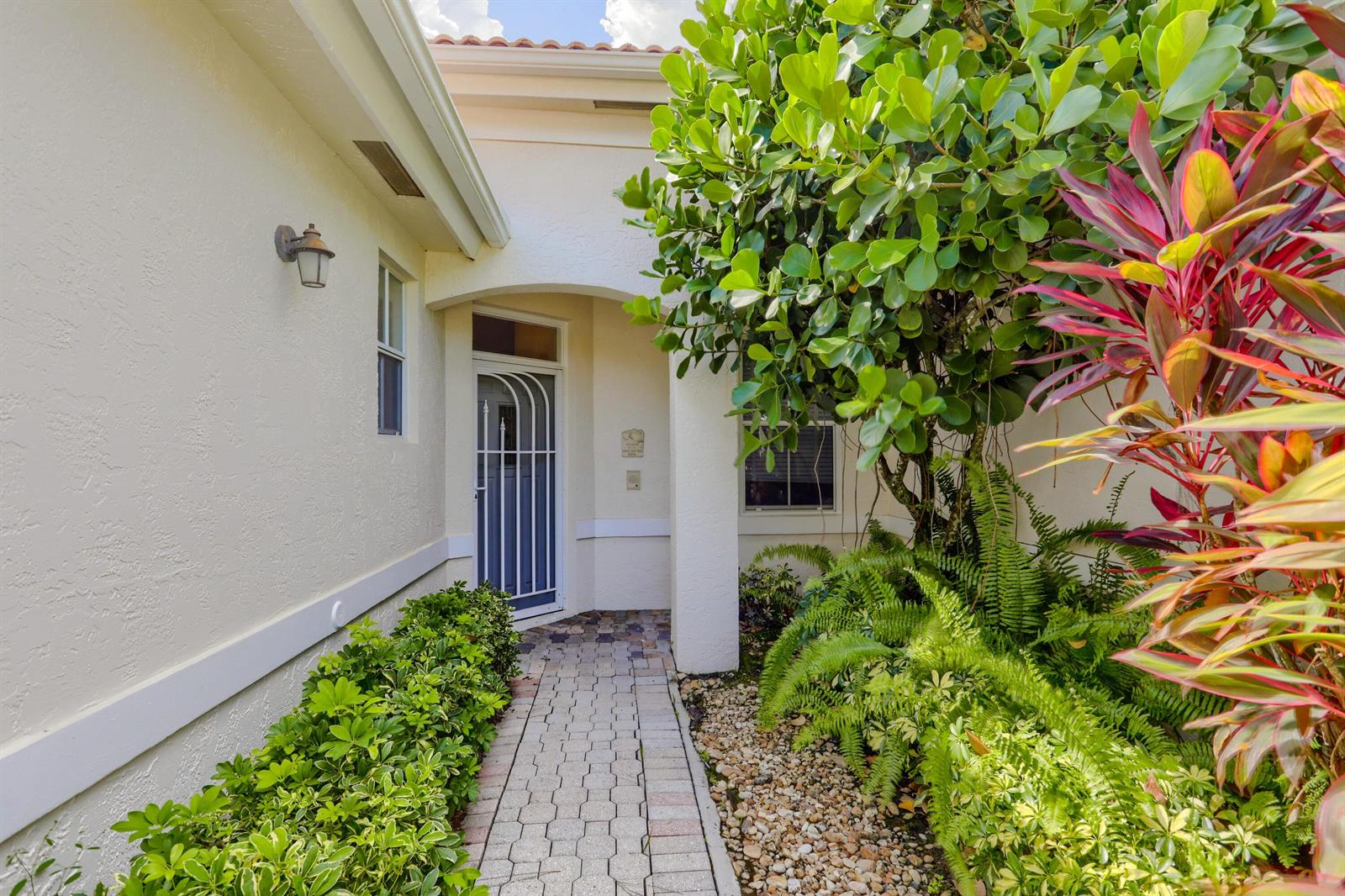 A paved walkway leads to a front entrance with a white security door and landscaping — 8193 Sandpiper Way, West Palm Beach FL 33412, WEST PALM BEACH, FL