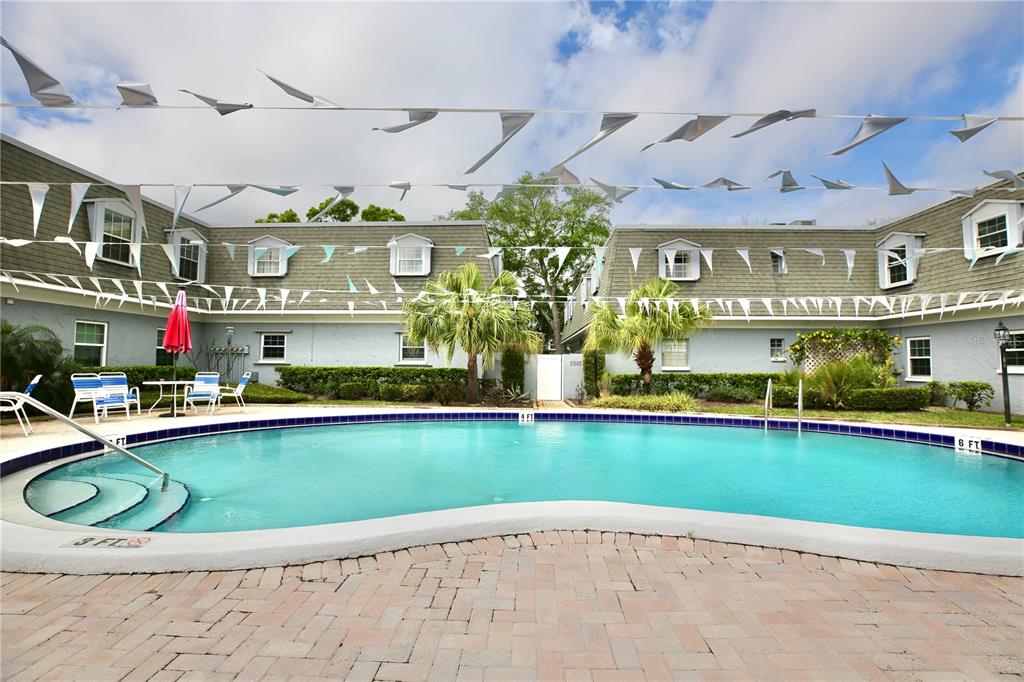 A swimming pool with a brick deck sits in front of a multi-story apartment building — 1713 BELLEAIR FOREST DRIVE UNIT C, BELLEAIR, FL