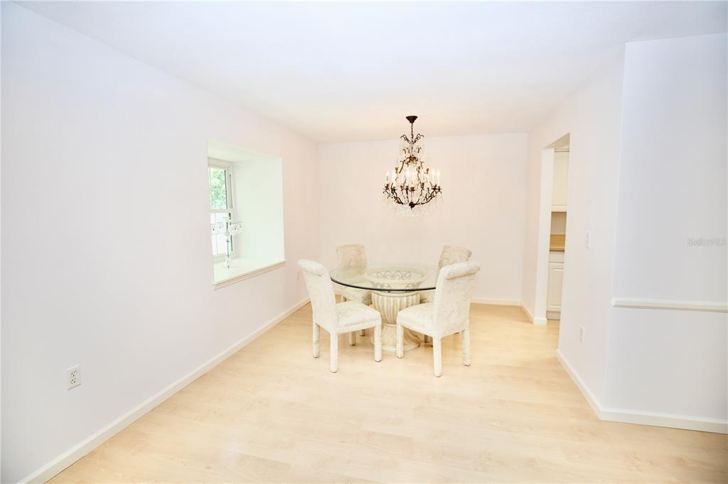 A dining room features a glass-topped table, upholstered chairs, and a large crystal chandelier — 1713 BELLEAIR FOREST DRIVE UNIT C, BELLEAIR, FL