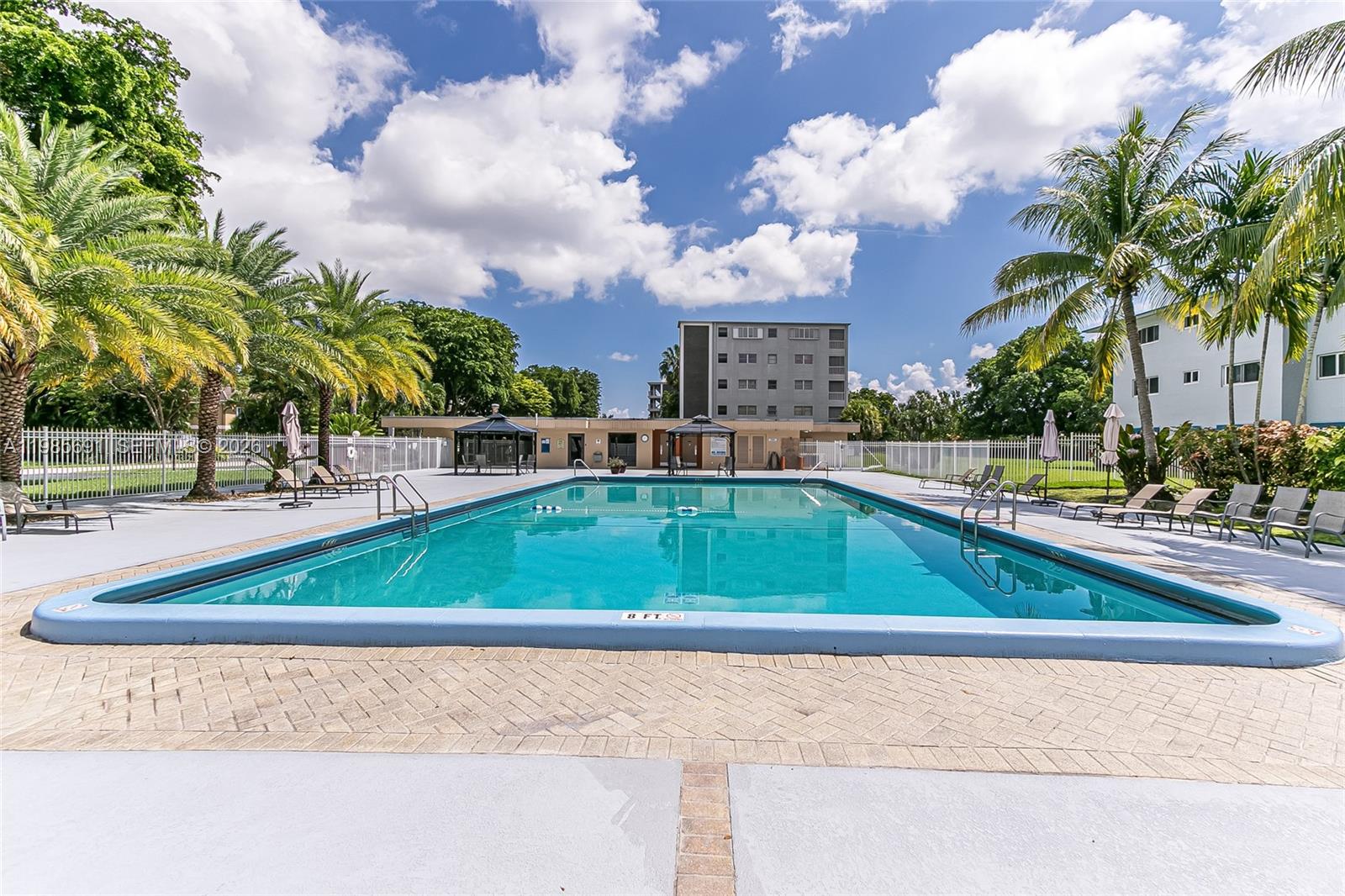 A rectangular swimming pool is surrounded by a paved deck, palm trees, and lounge chairs — 1000 Hillcrest Ct # 308, Hollywood FL 33021, HOLLYWOOD, FL