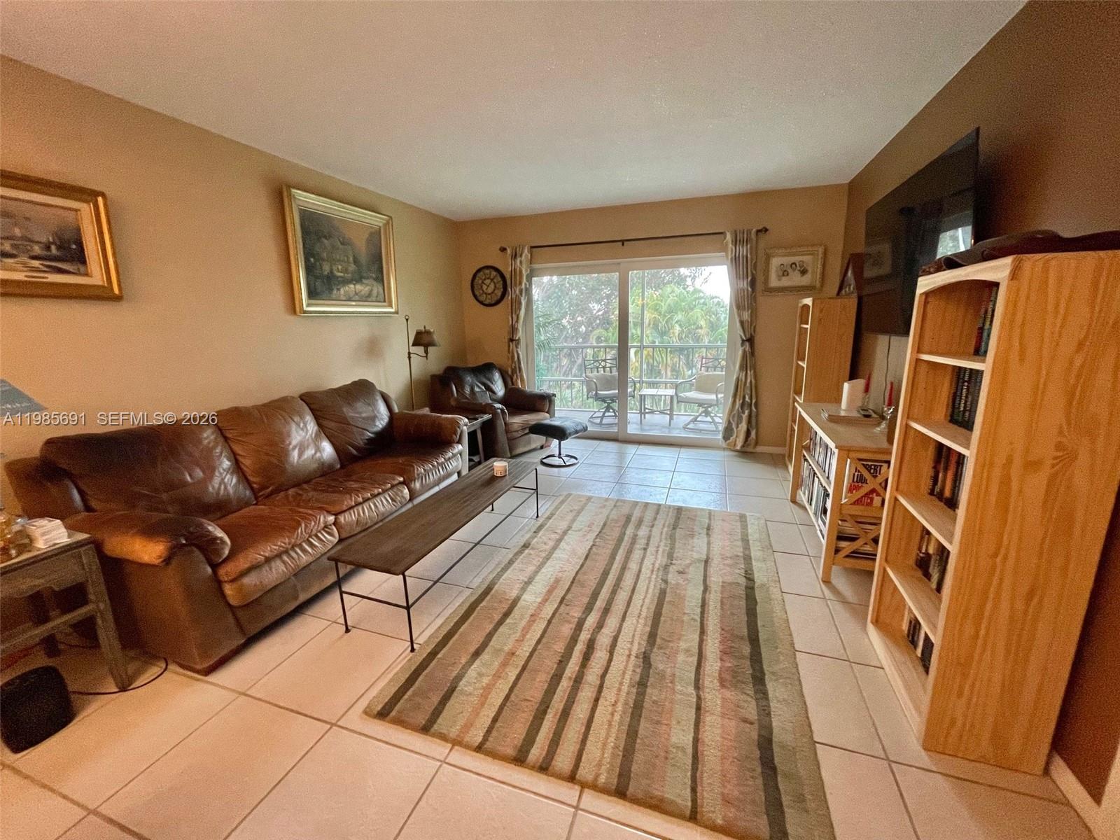 A living room features a brown leather sofa, a striped rug, and light-colored tile flooring — 1000 Hillcrest Ct # 308, Hollywood FL 33021, HOLLYWOOD, FL