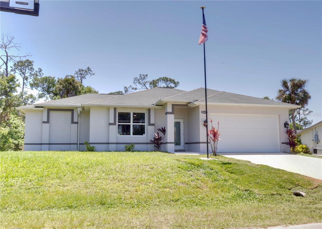 A single-story house with a light-colored exterior, a two-car garage, and an American flag — 22437 ADORN AVENUE, PORT CHARLOTTE, FL