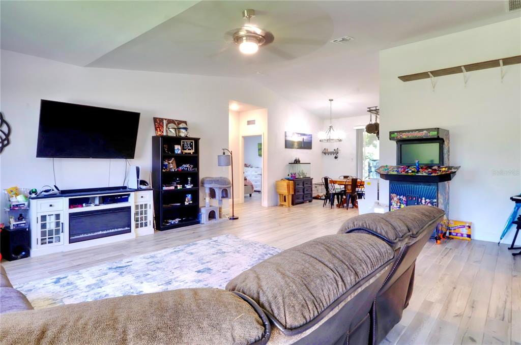 A living room features a large television, a gaming cabinet, and light-colored wood flooring — 22437 ADORN AVENUE, PORT CHARLOTTE, FL