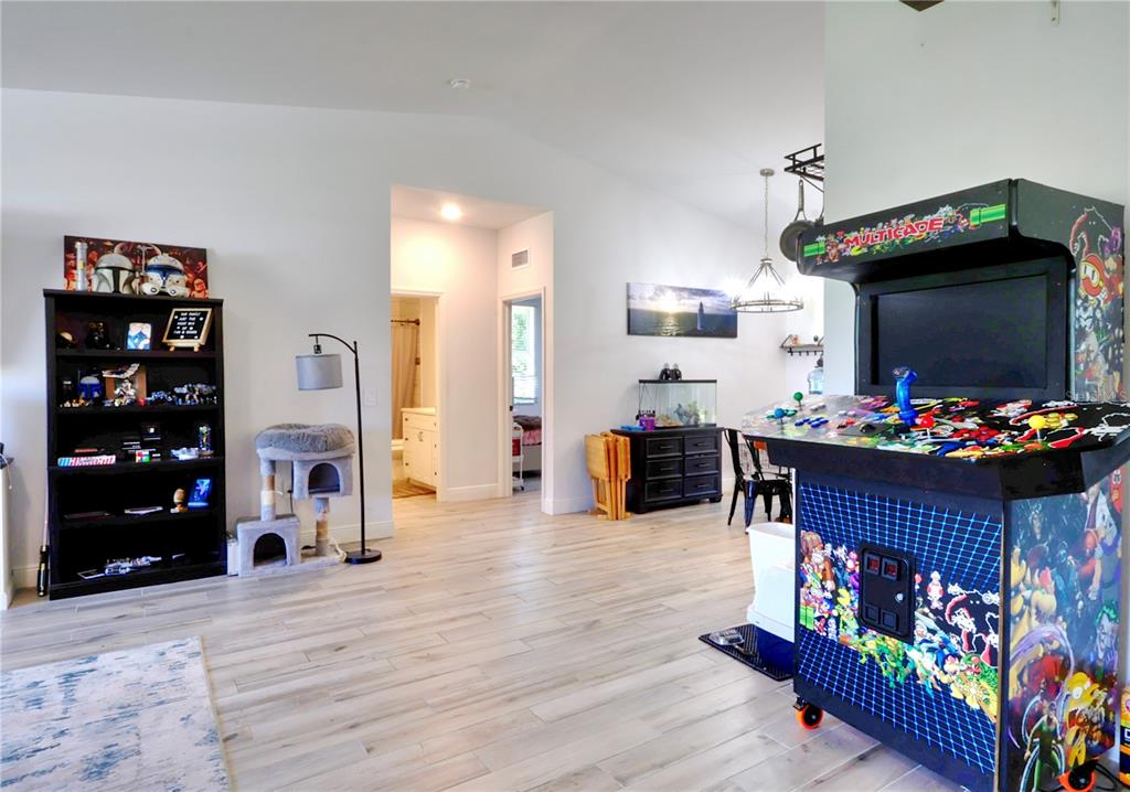 A living area features light wood-look flooring, a black bookshelf, and a large arcade cabinet — 22437 ADORN AVENUE, PORT CHARLOTTE, FL