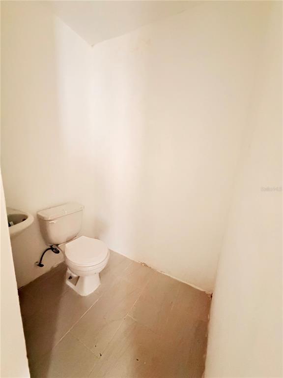 A small, minimalist bathroom features a white toilet, a corner sink, and light-colored floor tiles — Calle 601 BLOQUE 224 COMERCIAL 2, CAROLINA, PR