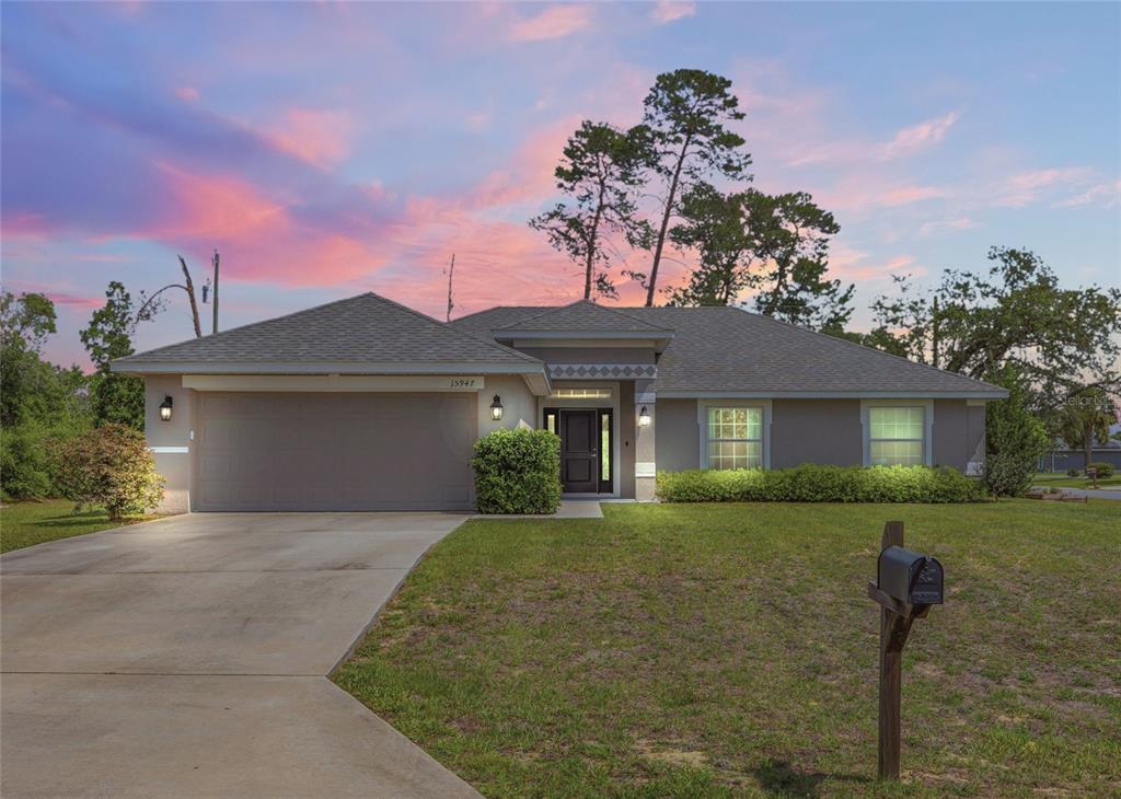 A single-story suburban house with a gray roof, tan stucco exterior, and a two-car garage — 15947 SW 26TH COURT, OCALA, FL