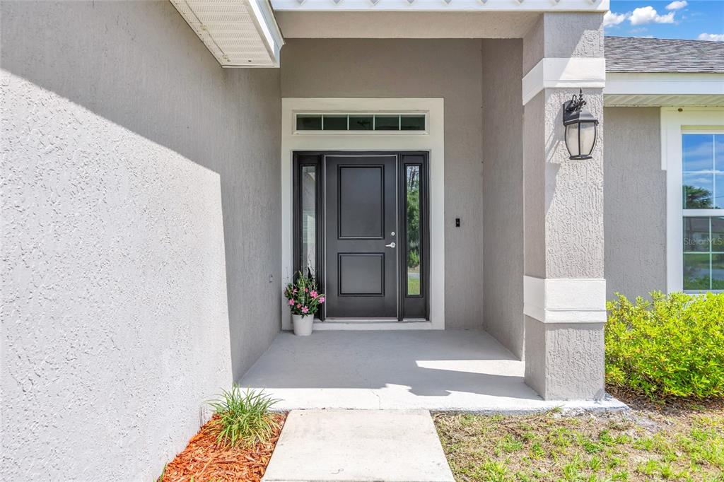 A gray stucco house exterior features a dark front door with sidelights and a transom — 15947 SW 26TH COURT, OCALA, FL