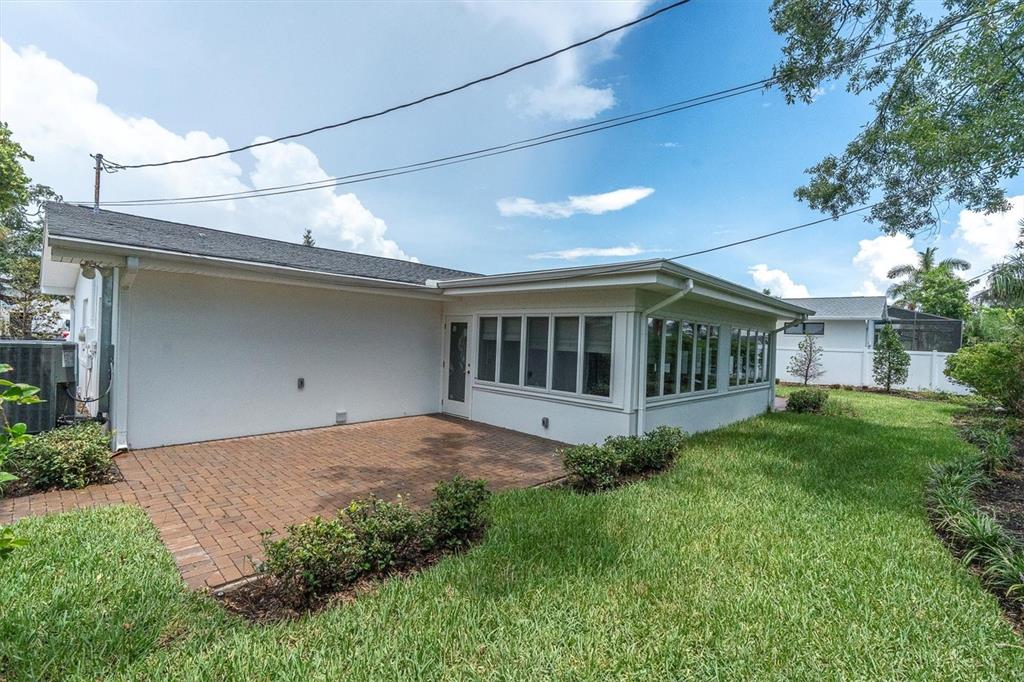 A brick patio sits beside a white house with a sunroom and a grassy yard — 319 RAFAEL BOULEVARD NE, ST PETERSBURG, FL