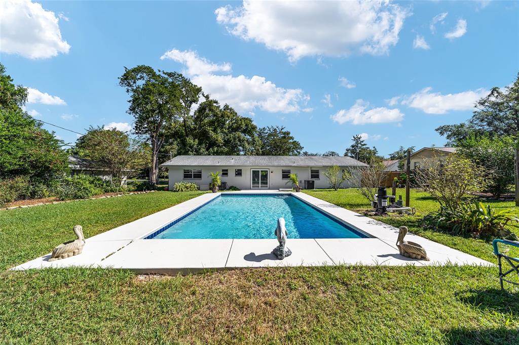 A rectangular swimming pool sits in a grassy backyard behind a single-story house — 3612 SE 34TH COURT, OCALA, FL