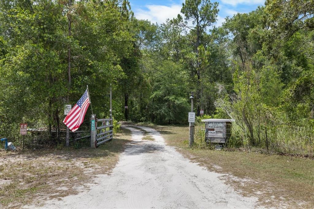 A dirt driveway leads through a gated entrance with an American flag and mailbox — 15624 PEACE BOULEVARD, SPRING HILL, FL