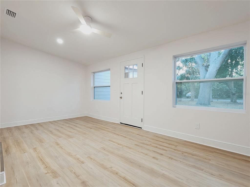 An empty room features light wood-look flooring, white walls, a ceiling fan, and exterior windows — 8917 N HIGHLAND AVENUE, TAMPA, FL