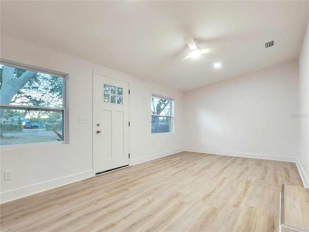A bright room features white walls, light wood-look flooring, a ceiling fan, and an exterior door — 8917 N HIGHLAND AVENUE, TAMPA, FL