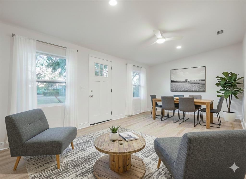 A living and dining room with light wood floors, gray chairs, and a wooden table — 8917 N HIGHLAND AVENUE, TAMPA, FL
