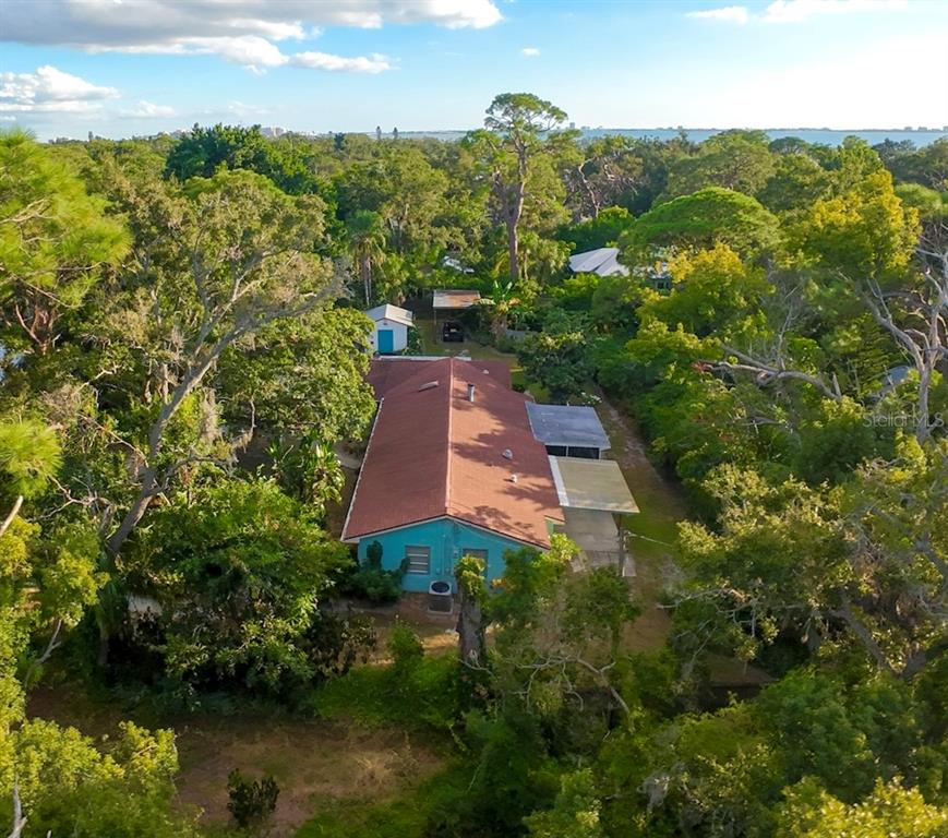 An aerial view of a teal house with a red roof surrounded by dense trees — 550 46TH STREET, SARASOTA, FL